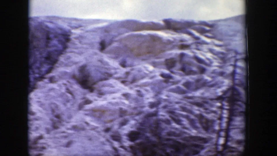 Snow-packed rounded terrain fills the frame, with sparse evergreens and soft 8mm color from the Wyoming 1939 home-movie clip.