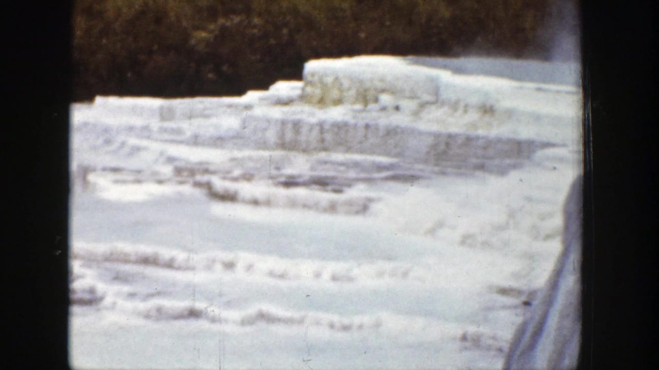 1939 Wyoming home-movie frame of frozen terraced formations, snow, and a dark wooded background.