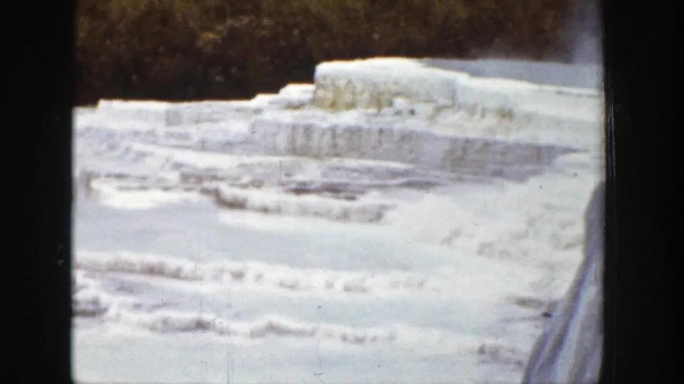 1939 Wyoming home-movie frame of frozen terraced formations, snow, and a dark wooded background.