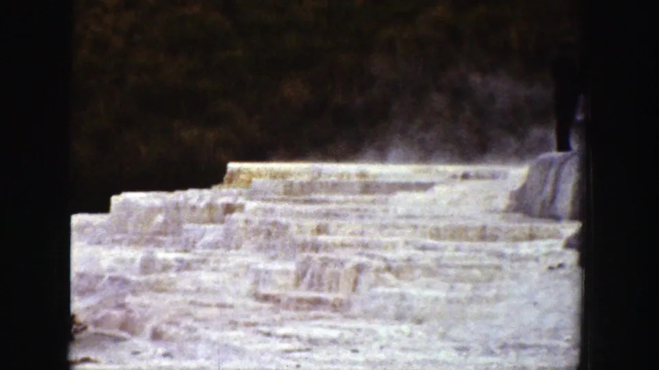 1939 Wyoming 8mm frame showing terraced frozen formations, possible steam, trees, and a distant standing visitor.