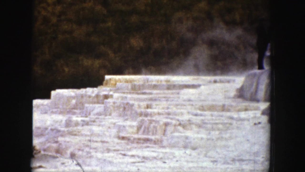Pale mineral terraces with steam rising and a dark figure near the upper edge.