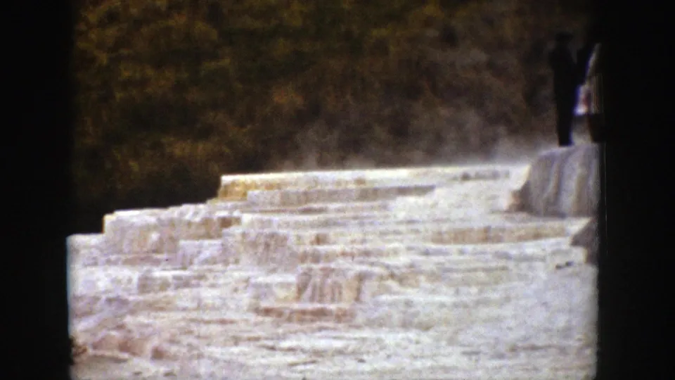 1939 Wyoming 8mm frame of a steaming terraced mineral formation, bordered by dark film edges and a small visitor near the top.