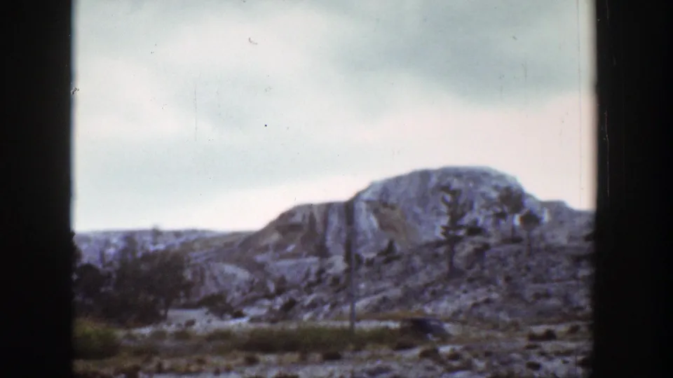Wyoming mountain view on 1939 8mm film, showing rocky slopes, patches of snow, sparse trees, and a cloudy sky.