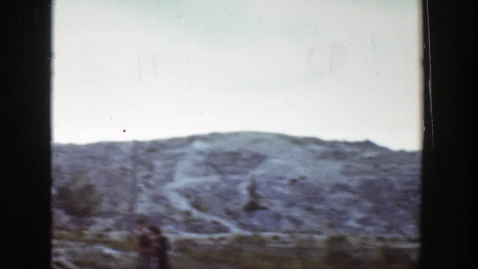 1939 Wyoming landscape showing a broad rocky slope, a faint path, scrub, and a small distant visitor near the foreground.