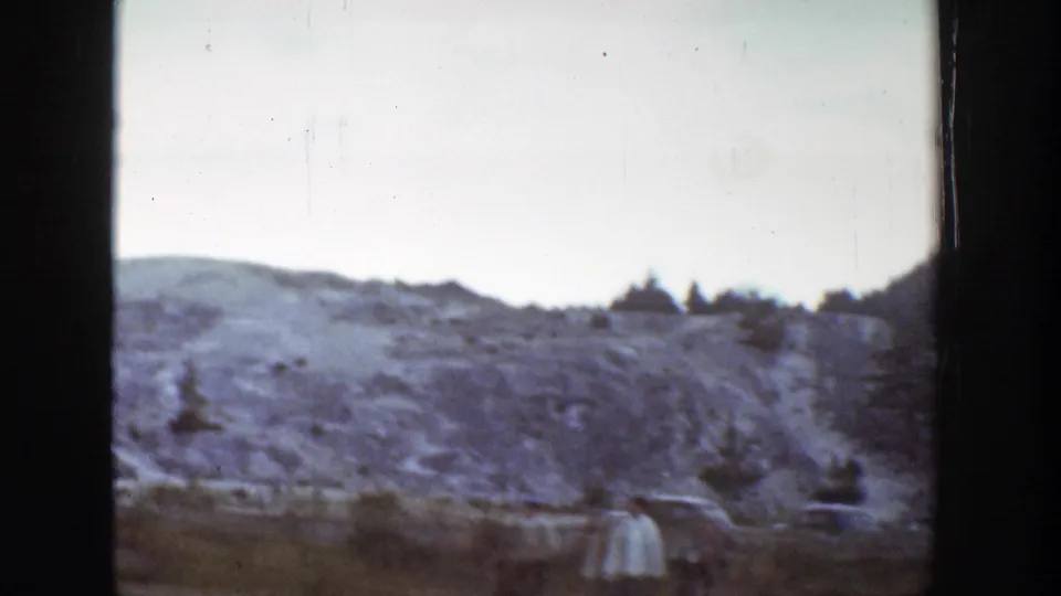 Soft 1939 8mm Wyoming view with a rocky hillside, sparse vegetation, and a distant visitor in light clothing at lower right.