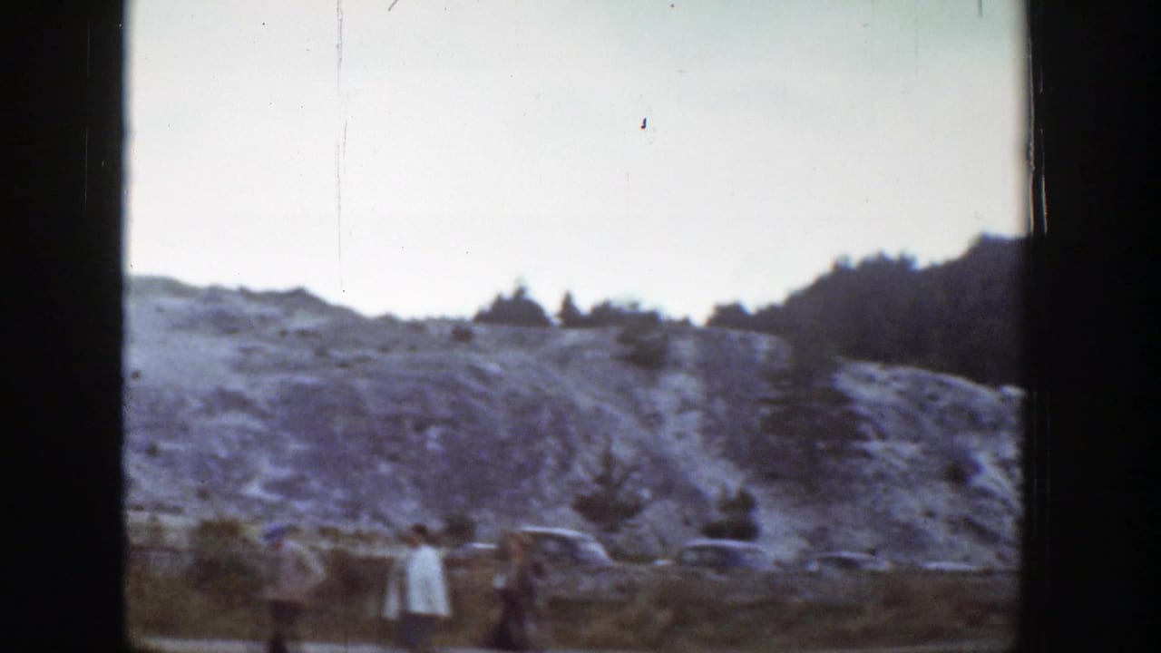 Visitors stand near a pale rocky hillside with trees and dark film gate edges.
