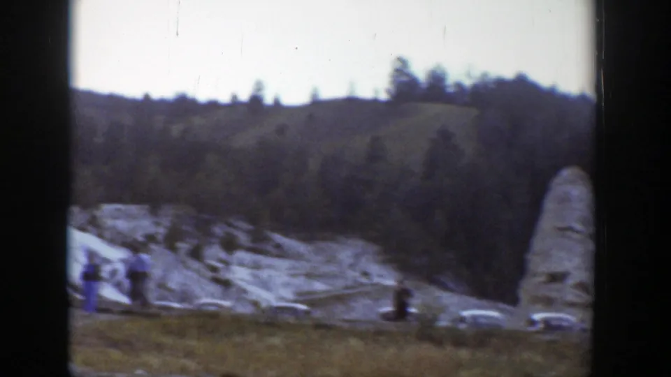 Home-movie view of tourists, cars, and a pale rock spire in a Wyoming mountain landscape.