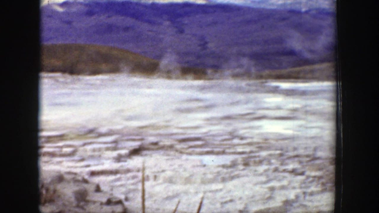 Open pale ground with distant hills and faint vertical steam or mist near the center.