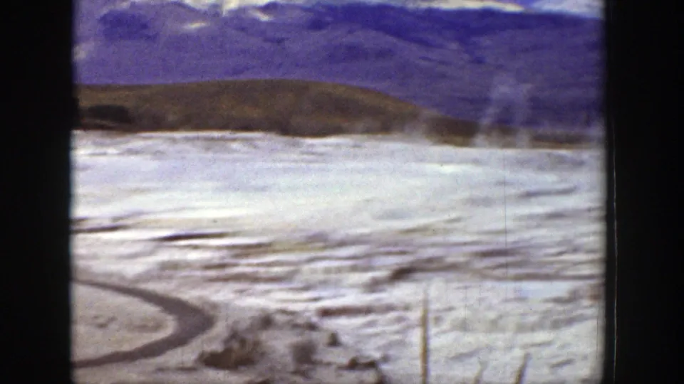 1939 Wyoming 8mm frame showing a pale barren flat, low hills, possible steam, sparse brush, and a curved foreground track.