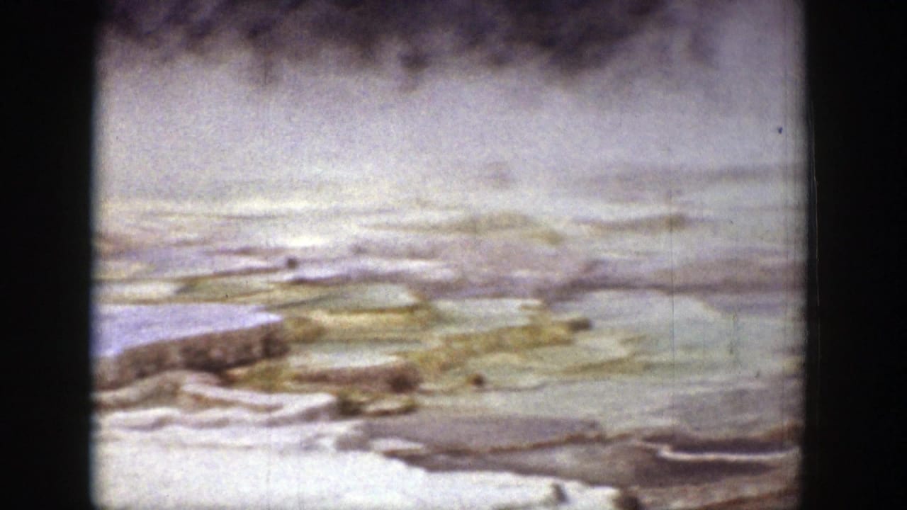 Soft view of hot spring terraces with steam drifting across pale mineral shelves.
