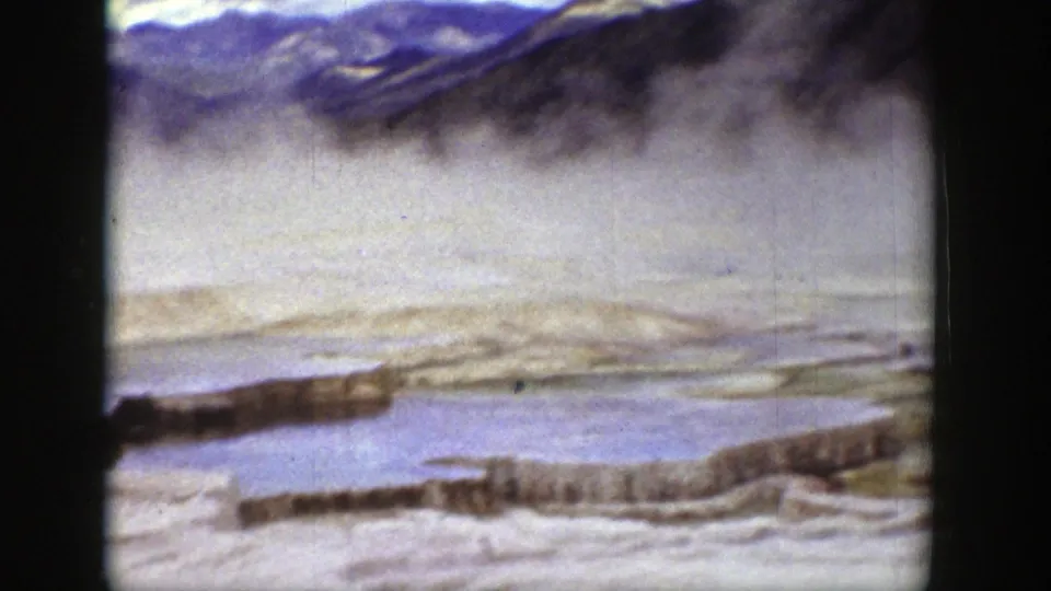 1939 Wyoming 8mm frame showing steaming mineral terraces, shallow water, and dark mountain forms in the background.