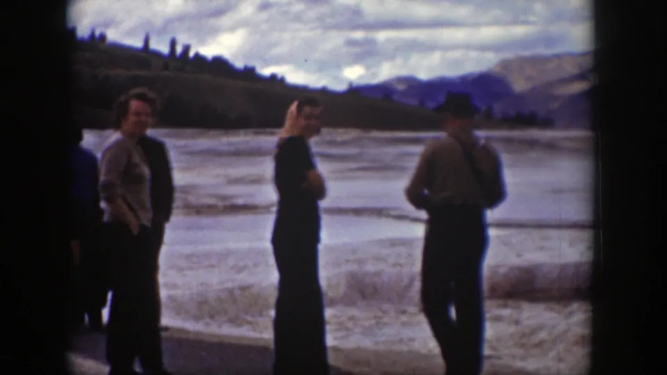 Adult tourists in 1939 Wyoming stand near a hot springs overlook, with steam, water, brush, and mountains in the background.