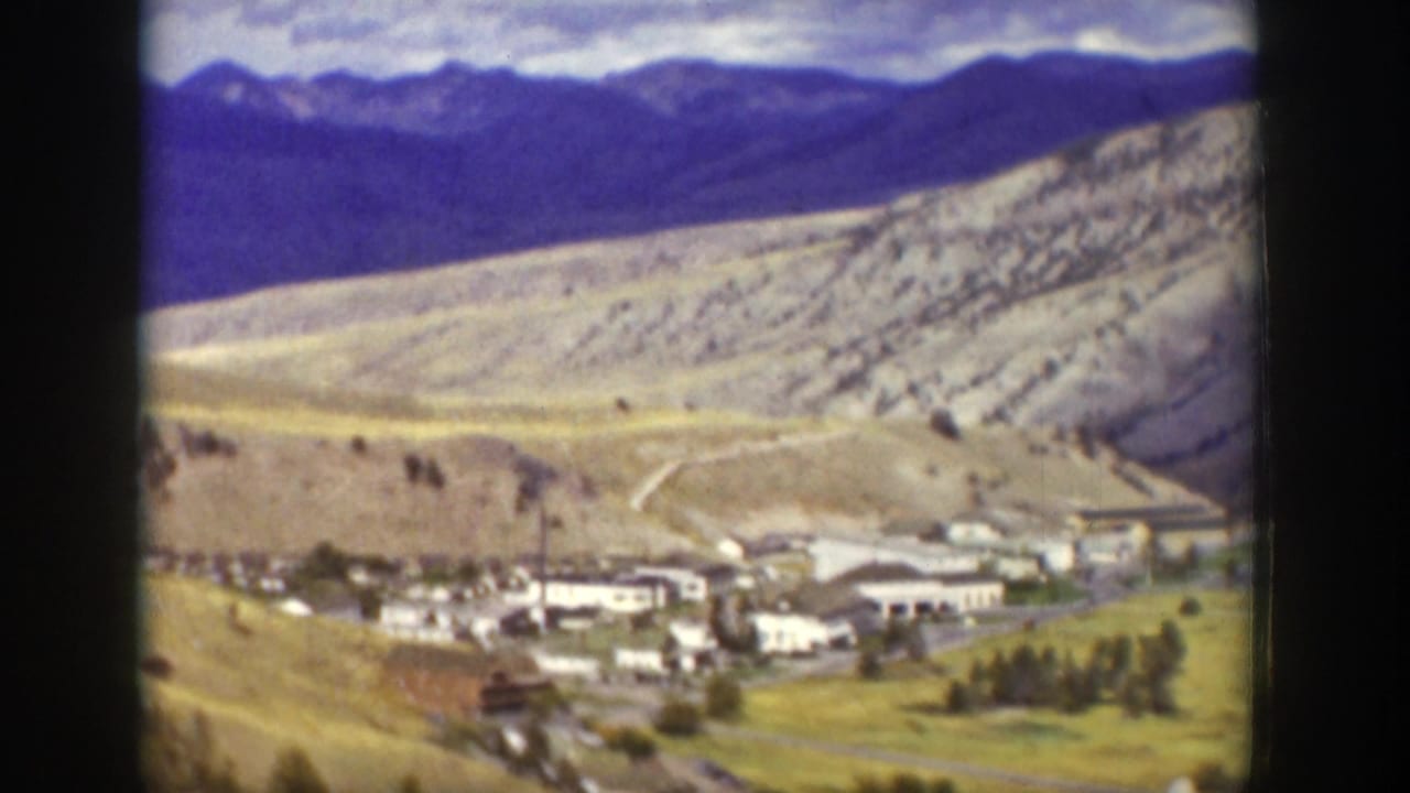 Mountain valley town seen from above with roads, trees, and distant ridges.