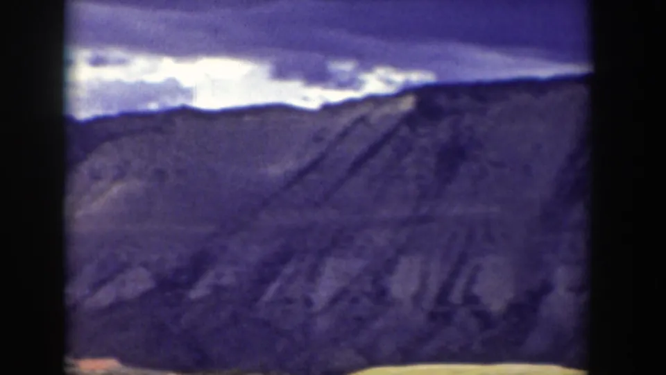 Soft 8mm landscape frame of a distant Wyoming mountain ridge under cloud cover, framed by dark contact-sheet edges.