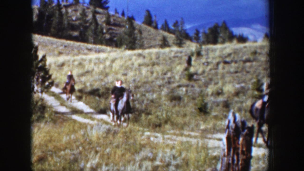 Horseback riders move along a dirt trail through grassy hills.