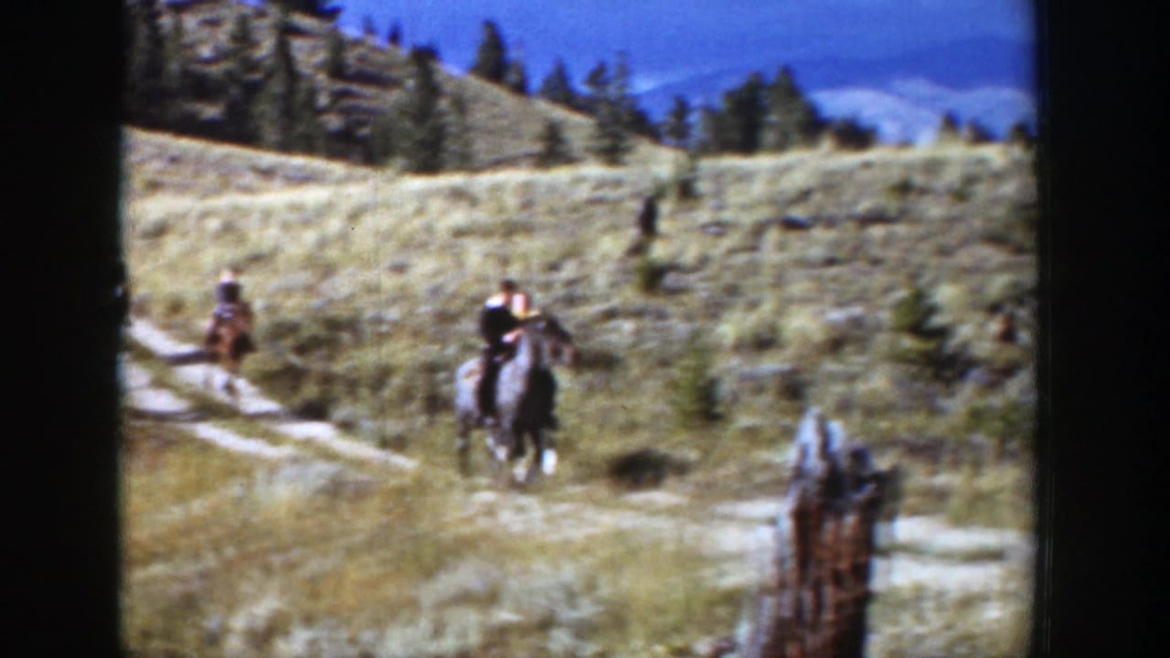 Several riders on horseback travel across an open hillside trail.