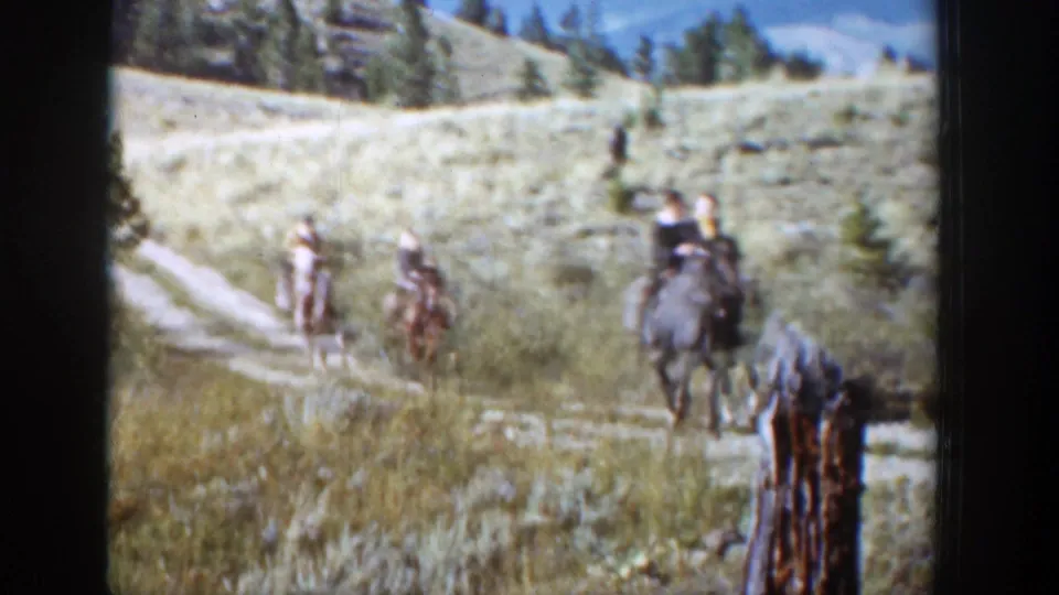 Horseback riders pass closer to the camera on a grassy Wyoming trail, with soft 8mm color and grain.