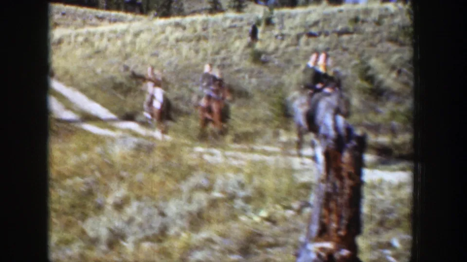 A rider on a gray horse passes close to a wooden post while other riders remain on the Wyoming mountain trail.