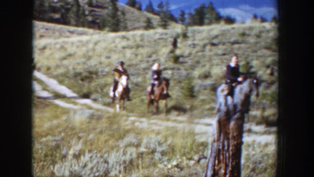 Three riders on horseback crossing a grassy open field near a dirt path.