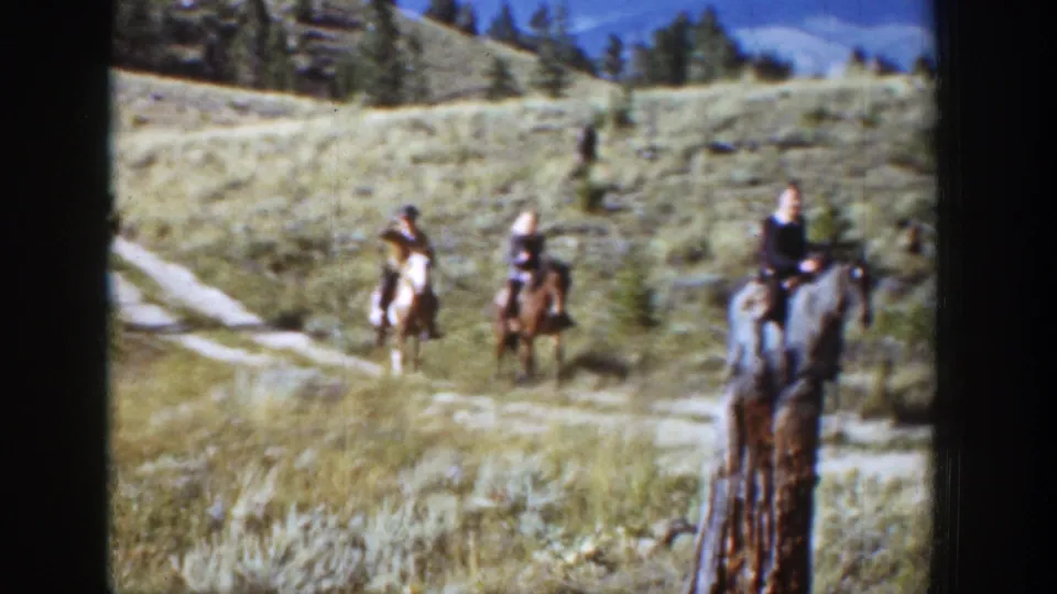 Three riders on horseback move through a sunlit Wyoming meadow in 1939 home-movie footage, with trees and open hillside behind them.