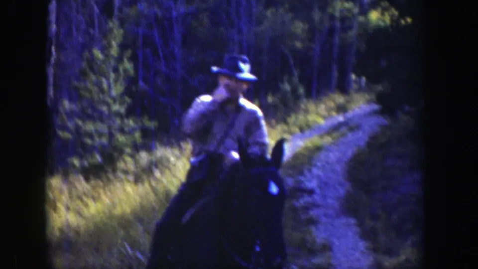 A hat-wearing rider on horseback follows a narrow dirt trail through shaded forest in the 1939 Wyoming home movie.