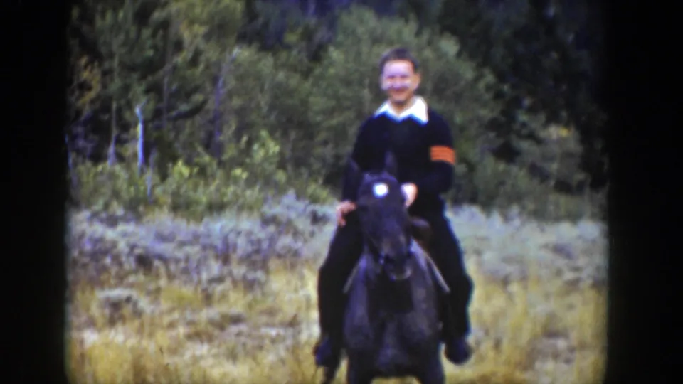 1939 Wyoming home-movie frame of a smiling adult rider on a dark horse, facing the camera in a wooded clearing.