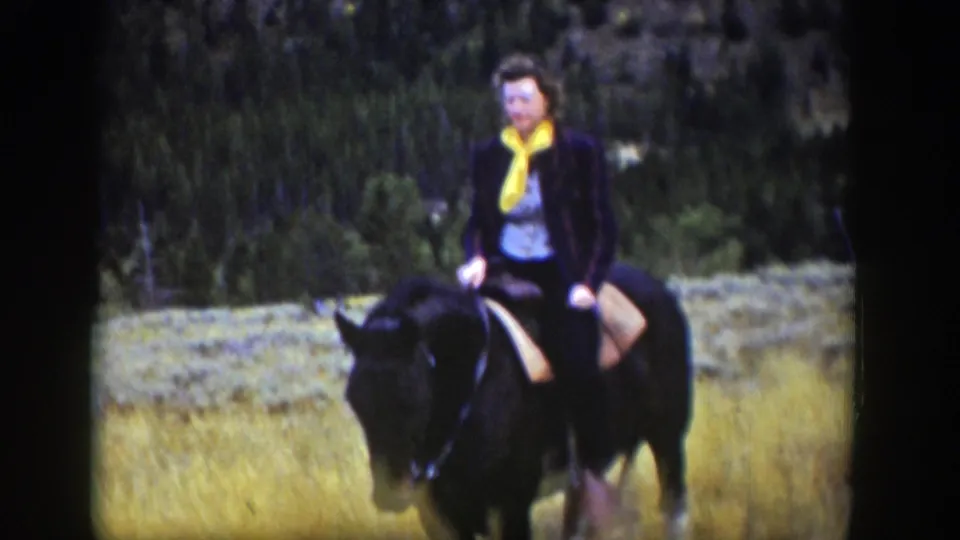 1939 Wyoming frame showing a woman with a yellow scarf mounted on a dark horse against trees and pale grass.
