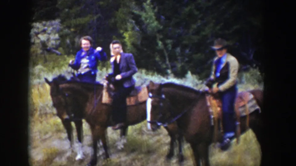 Three riders on horseback in 1939 Wyoming pause among trees and brush, with one woman appearing to wave toward the camera.