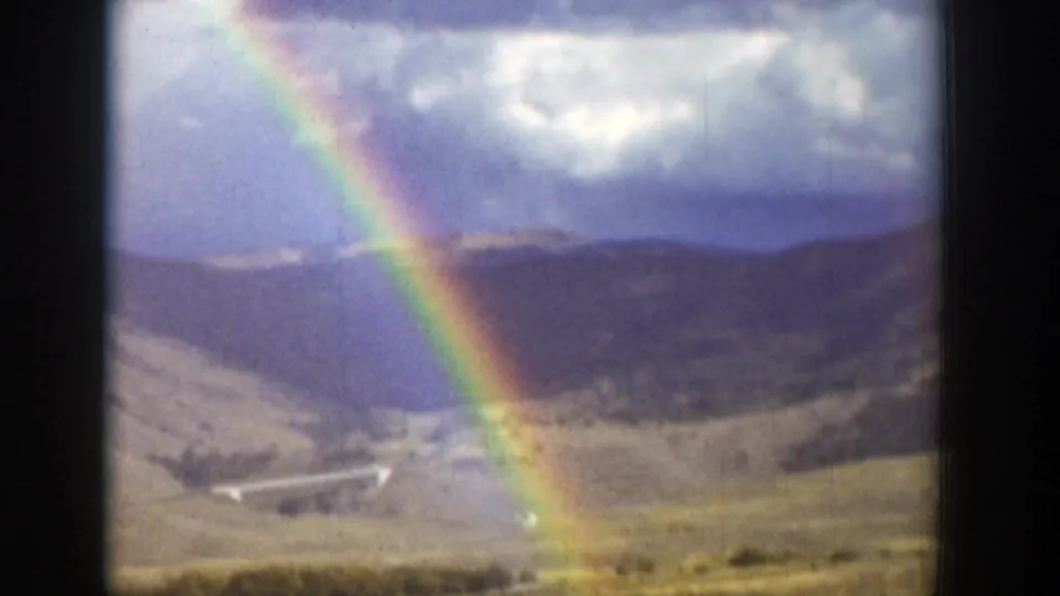 A vivid rainbow appears over a Wyoming valley, with mountains, clouds, and open fields visible through soft 8mm color.