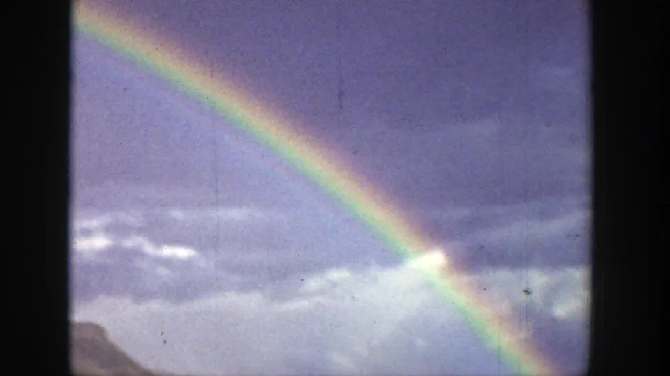A rainbow arcs across a cloudy Wyoming sky above a distant valley and mountain ridgeline in 8mm home-movie footage.