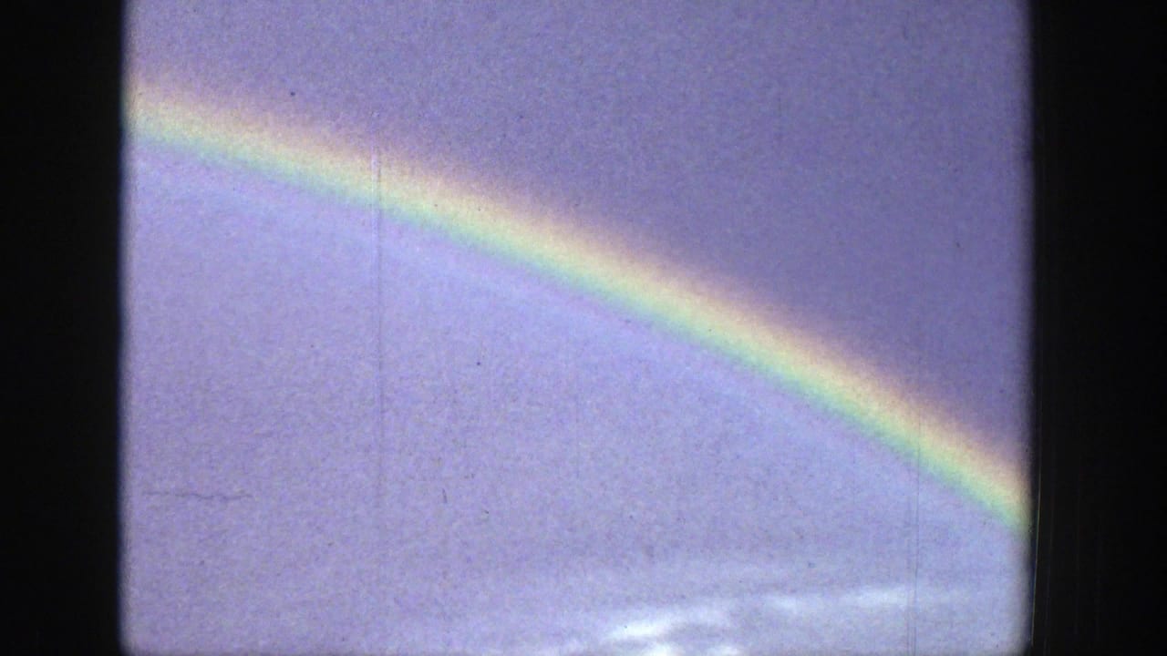 Rainbow segment against a cloudy blue-gray sky with film gate edges visible.