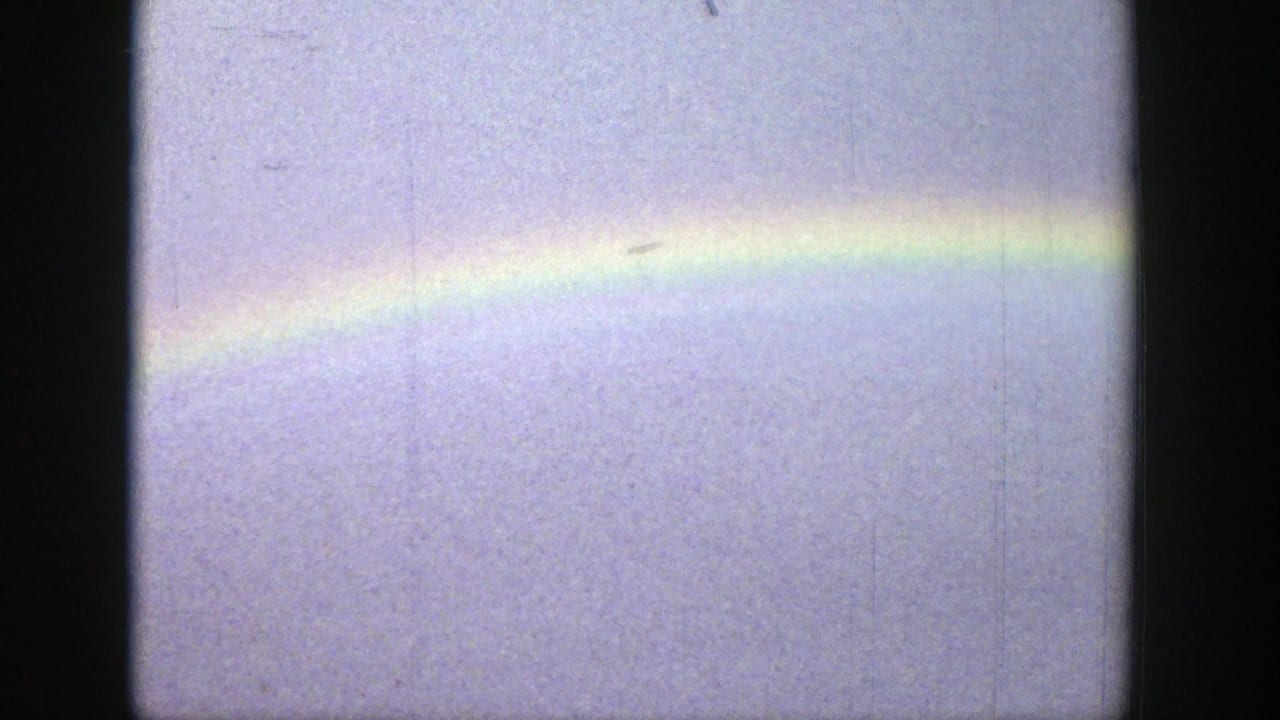 A faint rainbow segment spans the upper sky in the Wyoming landscape clip, framed by dark 8mm film edges.