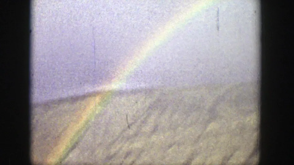 A rainbow drops toward open Wyoming hills in color 8mm footage, with haze, grain, and visible surface marks.