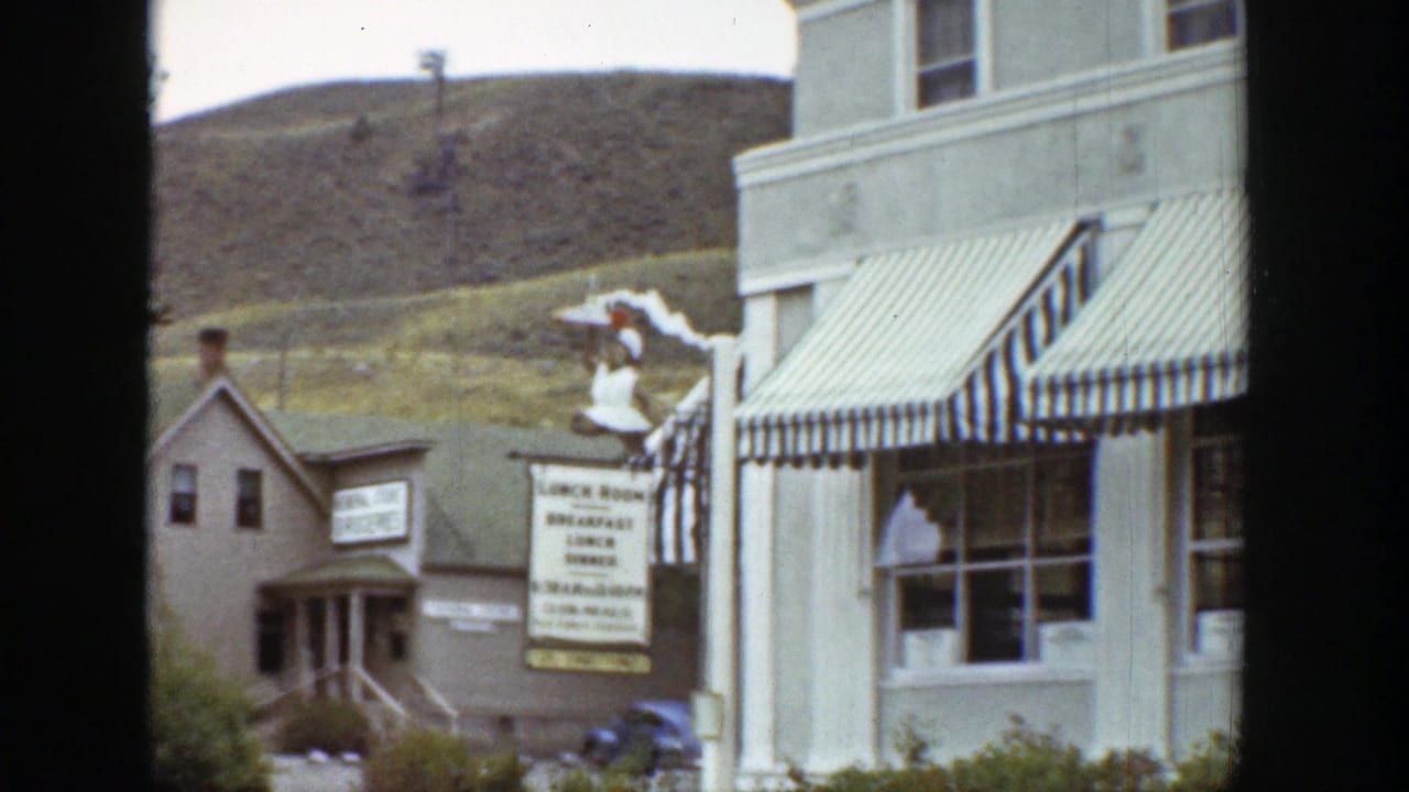 Small shop buildings with striped awnings, a lunch room sign, and hillside behind.