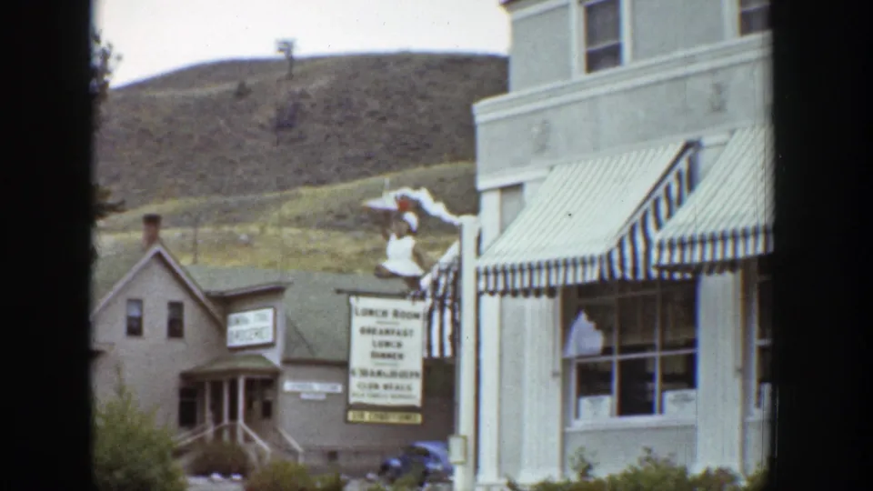1939 Wyoming frame showing commercial storefronts, a striped awning, a lunch room sign, and a hillside rising behind the shops.