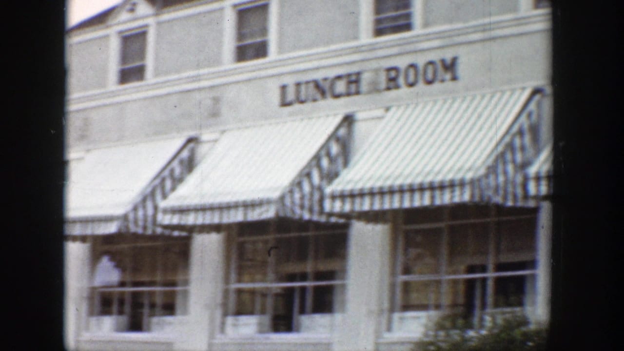 1939 Wyoming 8mm frame showing a white roadside lunch room with bold signage, striped awnings, and storefront windows.