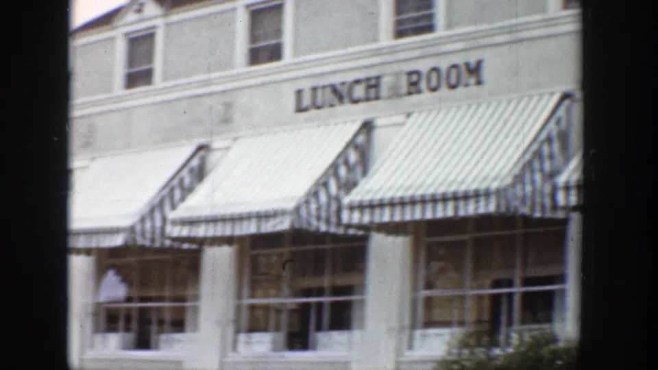 1939 Wyoming 8mm frame showing a white roadside lunch room with bold signage, striped awnings, and storefront windows.