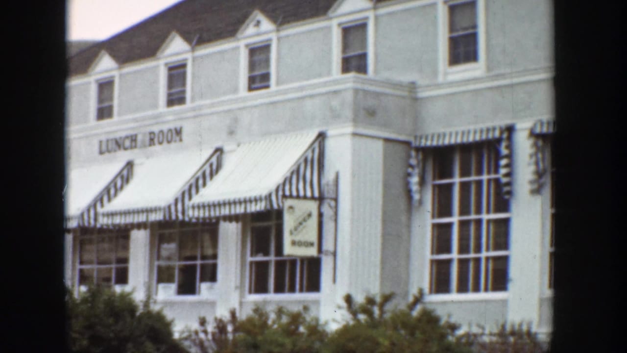 Wider 1939 Wyoming view of the white lunch room building, striped awnings, windows, and a smaller cocktail lounge sign.