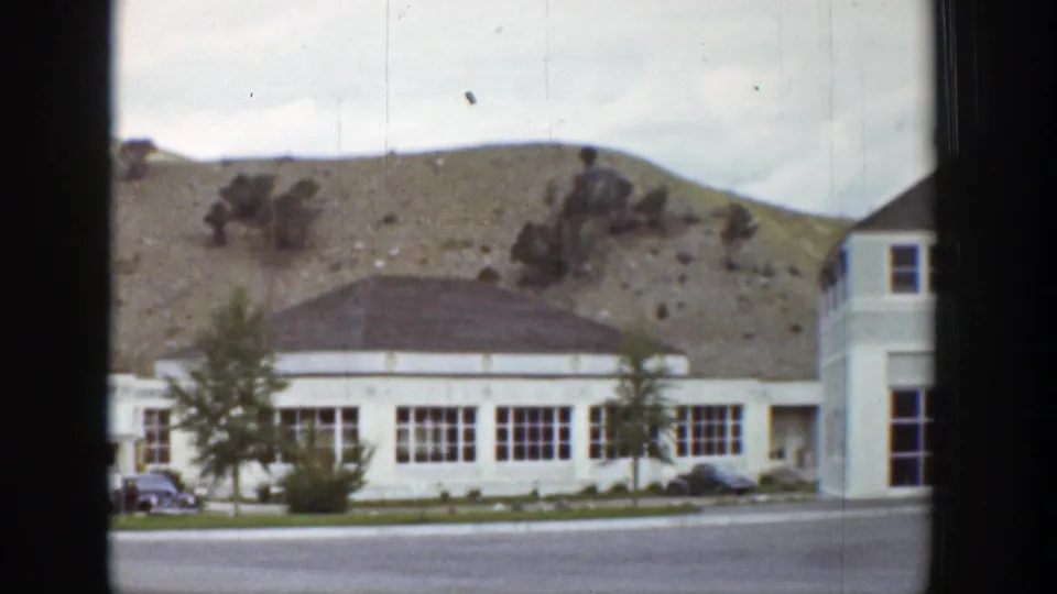 Late shot of the 1939 Wyoming roadside scene, showing the low white building, cars, trees, and dry hillside.