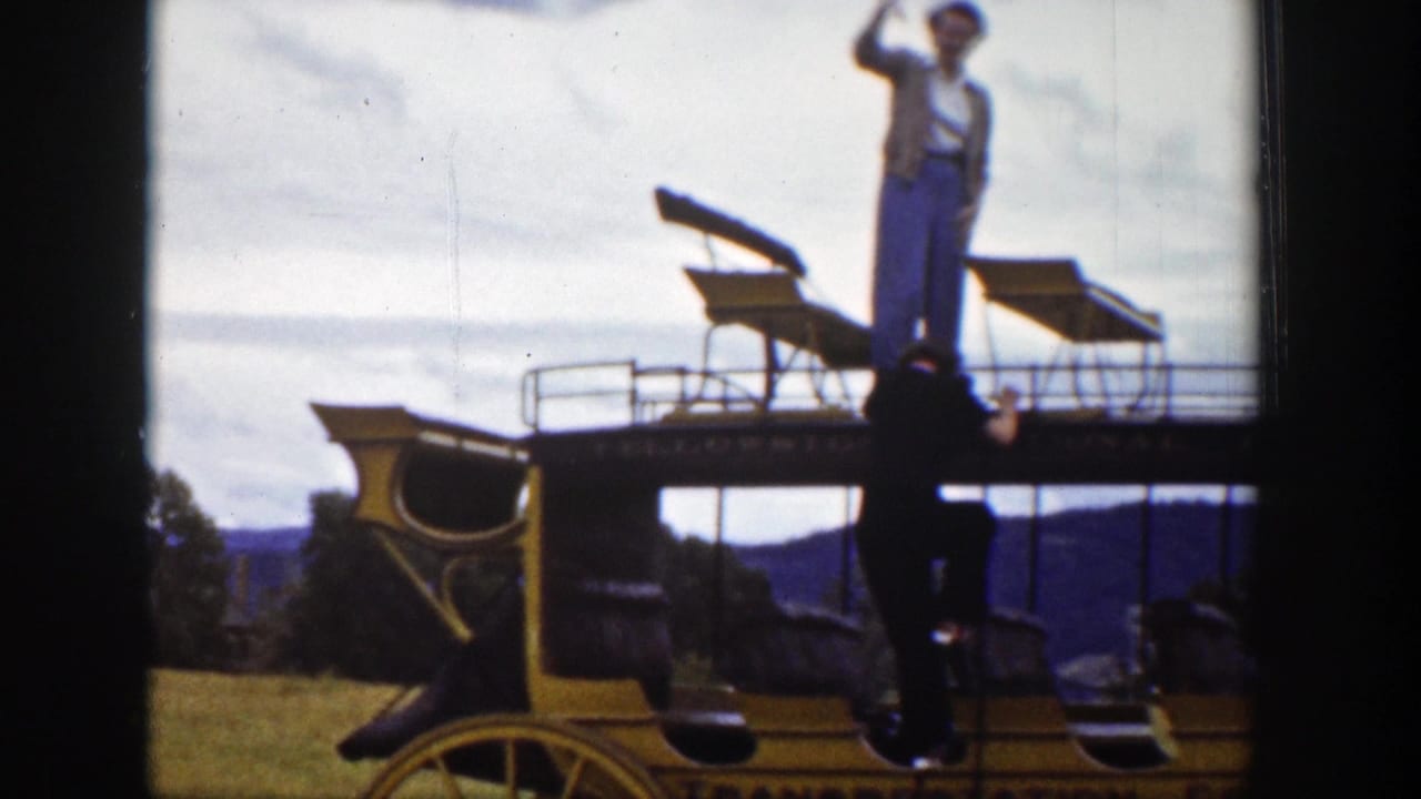 In 1939 Wyoming home-movie footage, a man waves from the top seat of a yellow stagecoach-style carriage in a rural landscape.