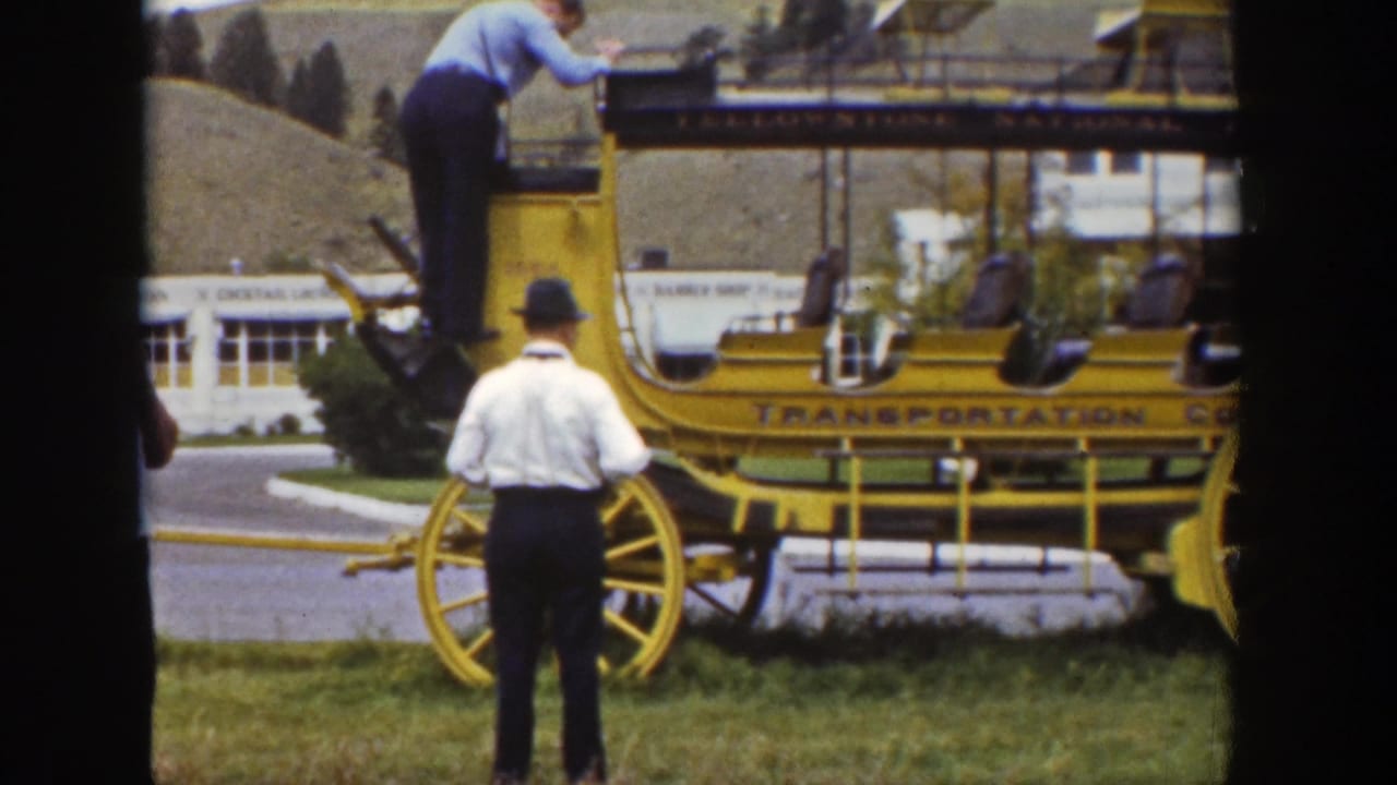 In 1939 Wyoming footage, a man in a blue shirt climbs on a yellow stagecoach as a man in a white shirt and hat stands on the grass.