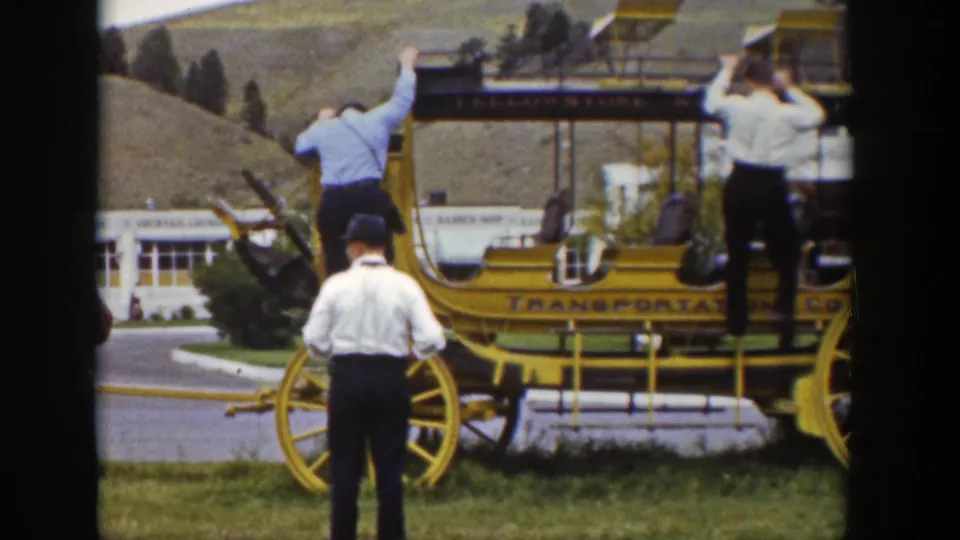Two adults climb on the yellow stagecoach as a man in a white shirt and dark hat stands below in the 1939 Wyoming footage.