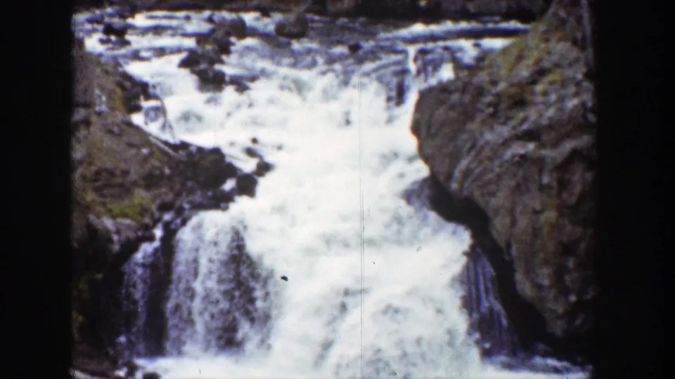 1939 Wyoming 8mm frame showing a compact waterfall and white rapids tumbling through rugged brown canyon rock.
