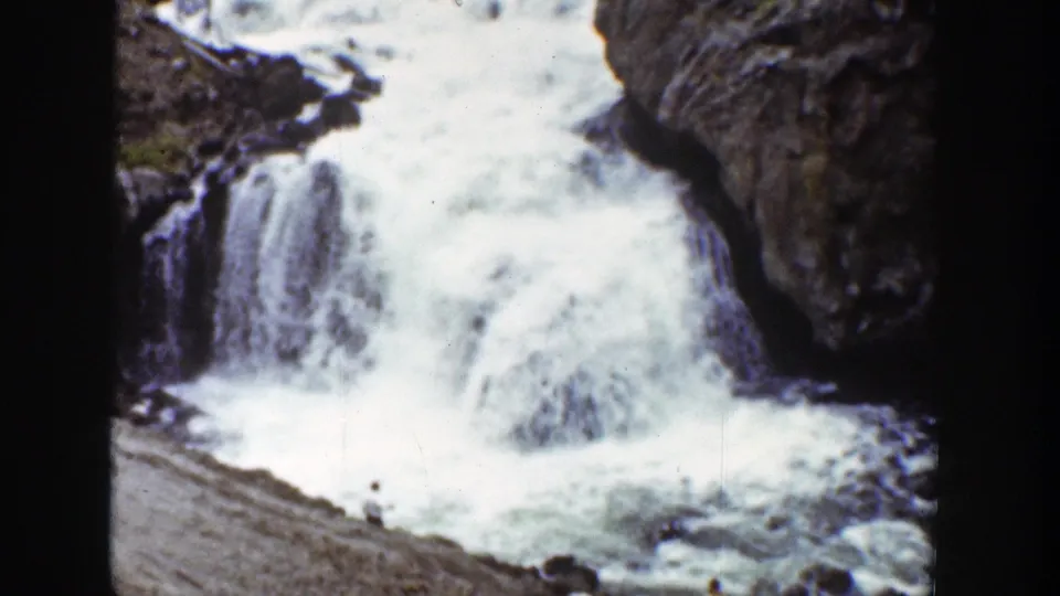 1939 Wyoming 8mm frame showing bright white water cascading over brown rocks beside a gravelly canyon bank.