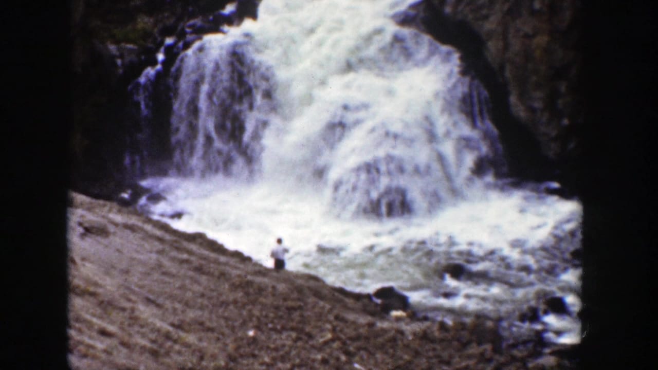 A waterfall pours into turbulent water with a distant person standing on the bank.