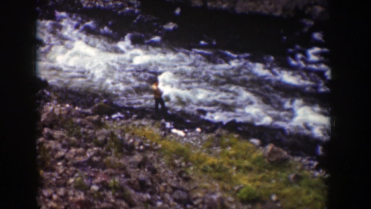 A distant person in brown clothing stands beside fast-moving river water in a Wyoming 1939 home-movie frame.