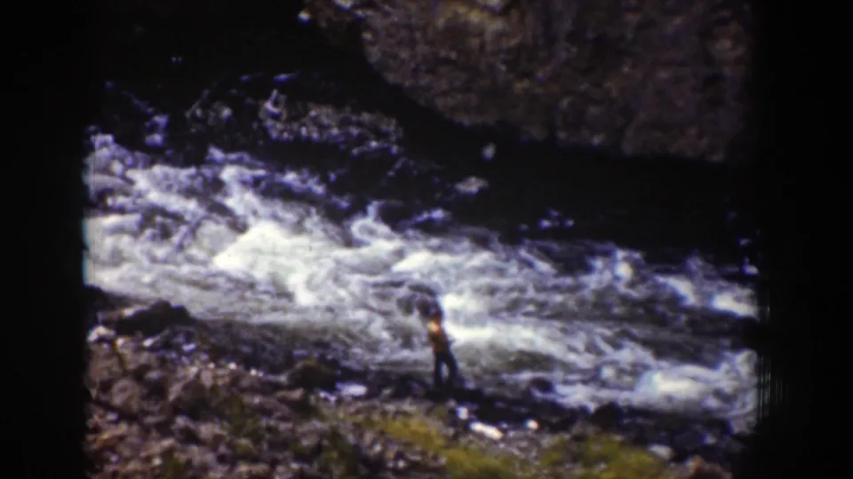 A distant person in a brown shirt stands beside rushing river water in this 1939 Wyoming 8mm home-movie still.