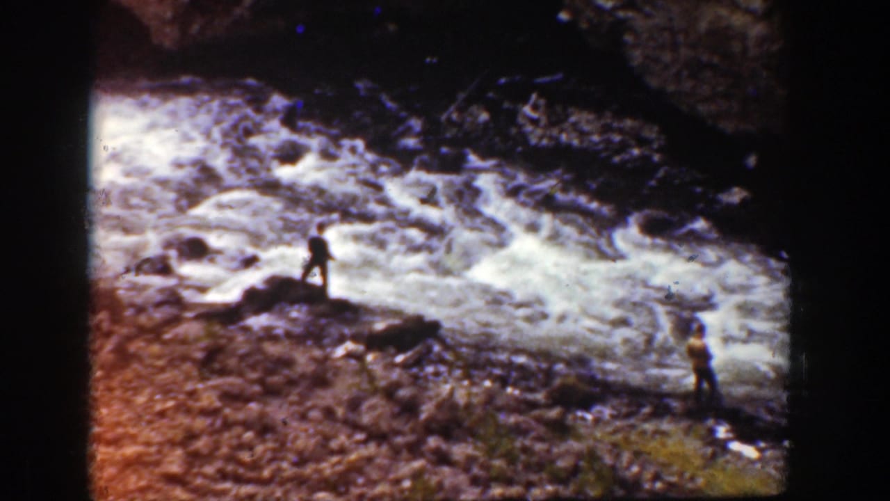 1939 Wyoming home-movie view of distant people near whitewater rapids and dark rocks.
