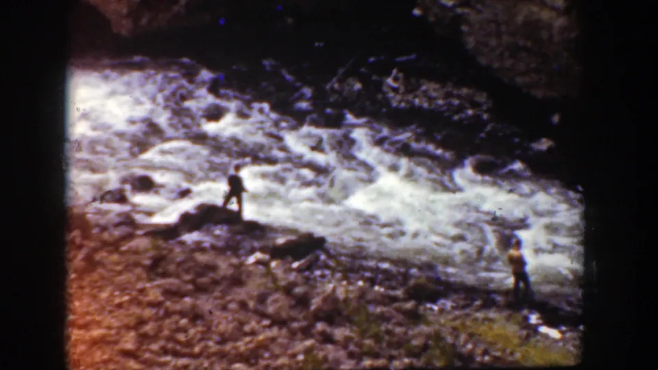 1939 Wyoming home-movie view of distant people near whitewater rapids and dark rocks.