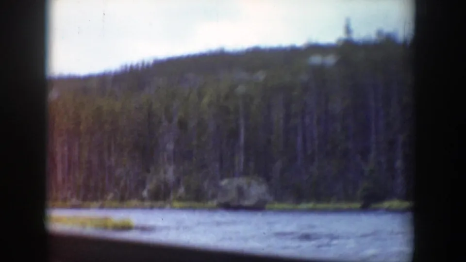 1939 Wyoming home-movie frame from a moving vehicle, with river water and forested hillside beyond the window.